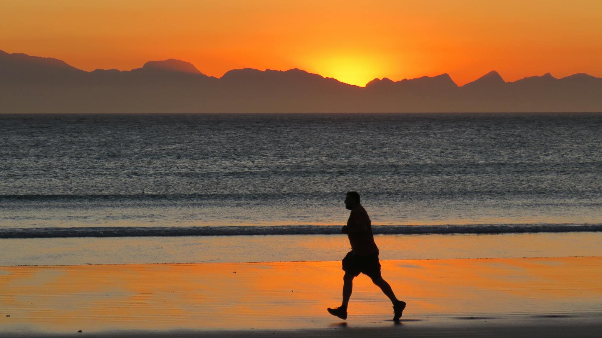 A jogger's silhouette along the shore at sunset