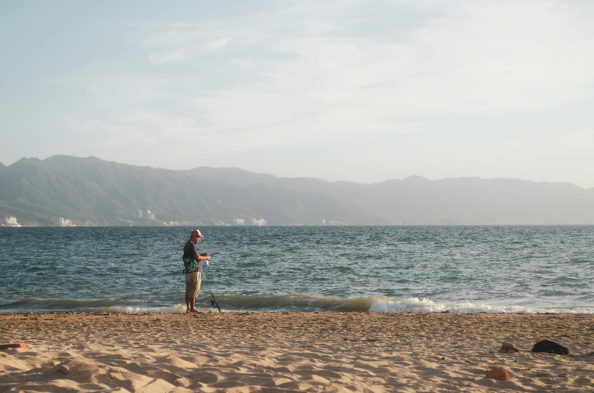 A fisherman on a calm Puerto Vallarta beach with mountains across the bay